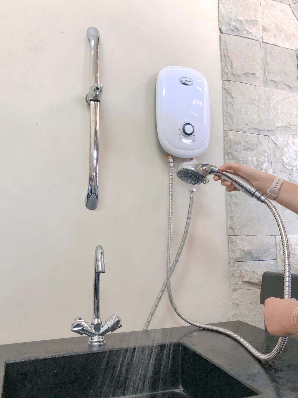 A woman holding a rose shower head connected to the e-cotherm tankless water heater