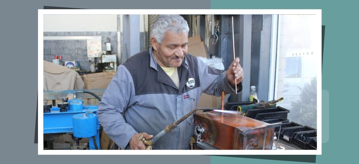 A technician hand-brazing a copper BlueWave boiling water tank at the E-Boil Systems workshop in Cape Town
